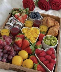 a wooden tray filled with fruit and veggies next to croissants