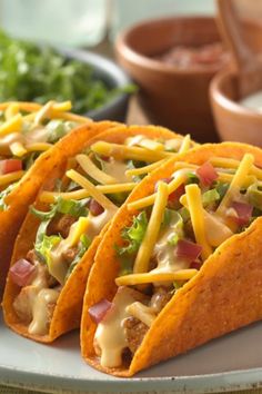 three tacos are sitting on a plate with condiments in bowls behind them