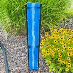 a blue vase sitting on top of a metal stand next to flowers and plants in a garden