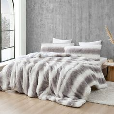 a bedroom with a large bed covered in grey and white blankets, pillows and rugs