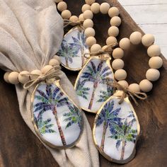 three wooden beads with palm trees painted on them are tied to a burlwood board