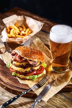 a hamburger and fries on a wooden tray with a glass of beer next to it