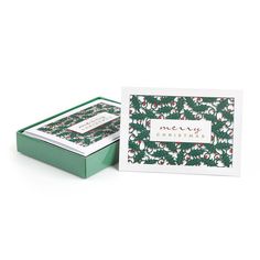 a christmas card in a green box with holly and berries on it, sitting next to a