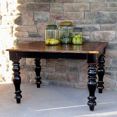 an old wooden table with jars and fruit on it in front of a brick wall