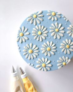 there is a blue and white cake with daisies on it next to some scissors