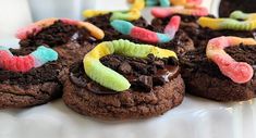 chocolate cookies decorated with candy worms and gummy worms on top of each cookie, sitting on a white plate