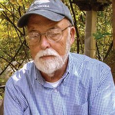 an older man with glasses and a hat is sitting in front of some trees looking at his cell phone