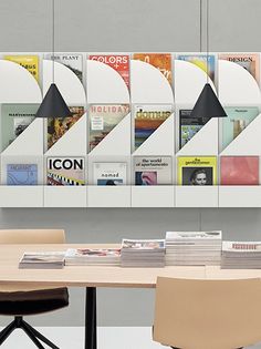 a wooden table topped with lots of books next to a wall mounted book shelf filled with magazines