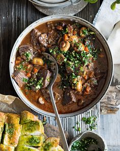 a pot filled with meat and vegetables next to some bread on a plate, along with other dishes