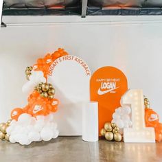 an orange and white balloon arch with the number one on it, along with other balloons