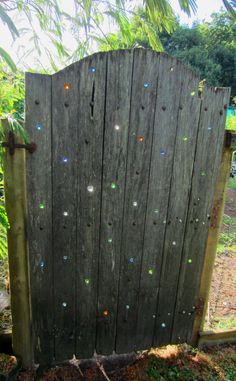 an old wooden gate with many colored dots on the board and in between it is a small patch of grass