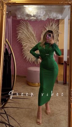 a woman in a green dress taking a selfie with her cell phone while standing in front of a mirror