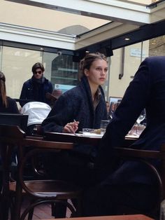 a woman sitting at a table with food in front of her and other people standing around