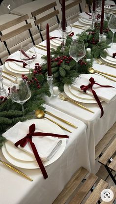 the table is set with white plates, silverware and greenery for christmas dinner