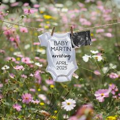 a baby bodysuit hanging on a clothes line in a field of flowers