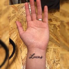 a person's hand with the word lucas written on it and a small wrist tattoo