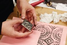 a person is stamping something on a piece of pink paper with black and white designs