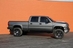 a silver truck parked in front of a brick wall with black rims and tires