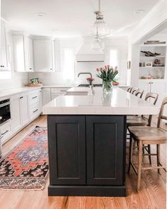 a large kitchen with an island in the middle and chairs at the end, along with a rug on the floor