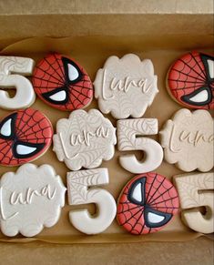 decorated cookies in the shape of spiderman's faces and numbers are displayed on a cardboard box