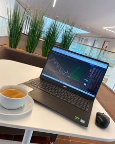 a laptop computer sitting on top of a white table next to a cup of coffee