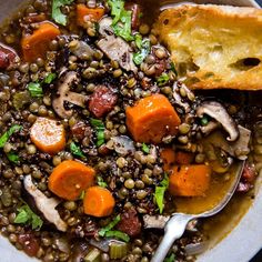 a bowl filled with lentils, carrots and other vegetables next to a piece of bread