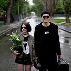 a man and woman are walking down the street with luggage, holding plants in their hands