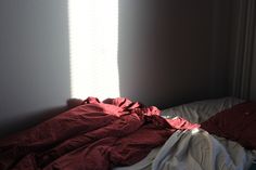 an unmade bed with red sheets and white sheets on it in front of a window