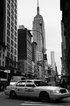 a taxi cab is stopped at an intersection in new york's financial district, with the empire building in the background