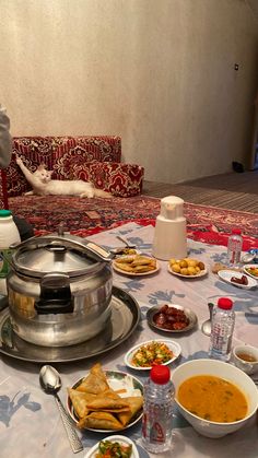 a table topped with bowls and plates filled with food next to a person sitting on a couch