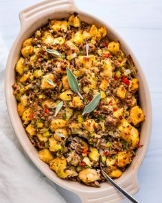 a casserole dish filled with stuffing, vegetables and sage sprigs next to a fork