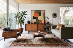 a living room filled with furniture and lots of windows next to a large painting on the wall