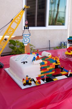 a birthday cake made out of legos on a table with a crane in the background