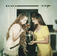 two young women holding a cat and looking at a large metal bowl in front of them