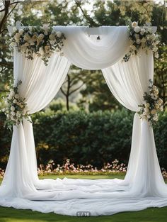 an outdoor wedding ceremony with white draping and flowers on the altar, surrounded by greenery