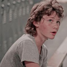 a young boy with curly hair sitting on a bench and looking at something off to the side