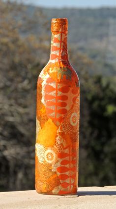 an orange bottle sitting on top of a wooden table next to some bushes and trees