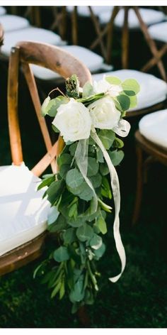 white roses and greenery are tied to the back of chairs