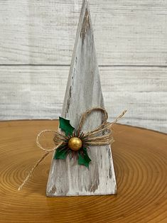 a small wooden christmas tree decoration on top of a wood table with twine and bells