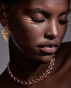 a woman with gold makeup and jewelry on her face, looking down at the camera