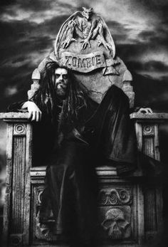 a black and white photo of a man with long hair sitting on a bench in front of a statue