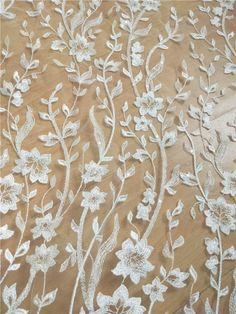 an embroidered fabric with white flowers and leaves on a brown background in close up view