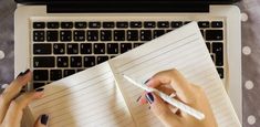 two hands writing on lined paper next to a laptop