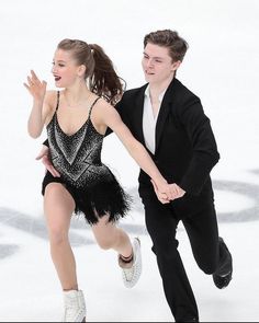 a man and woman skating on an ice rink in formal attire, one holding the other's hand