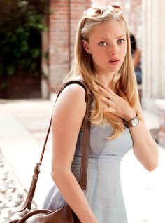 a woman in a blue dress carrying a brown purse and looking at the camera with her hand on her shoulder