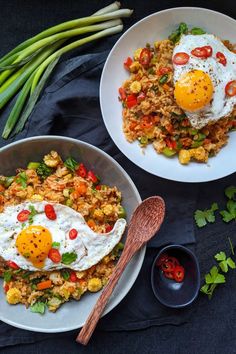 two plates filled with fried eggs and vegetables next to green beans on a black cloth