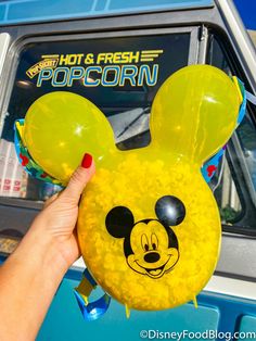 a person holding up a yellow mickey mouse balloon