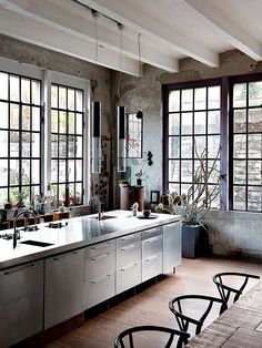 an industrial style kitchen with stainless steel appliances and large windows, along with wooden flooring