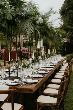 a long table is set with white plates and place settings for an outdoor dinner party