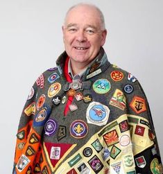 an older man wearing a jacket with many patches on it and smiling at the camera